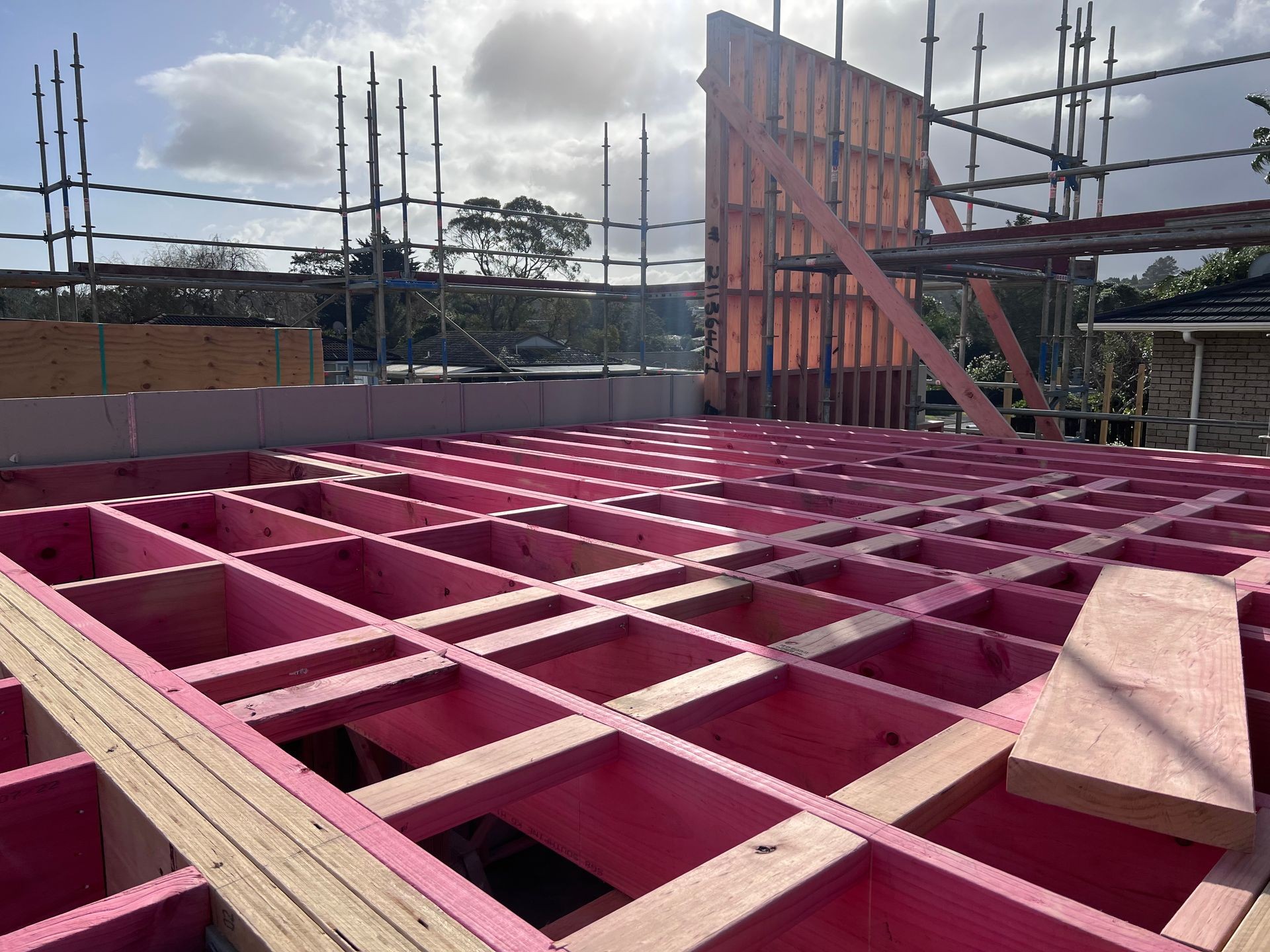 Construction site with pink wooden beams and scaffolding under a cloudy sky.