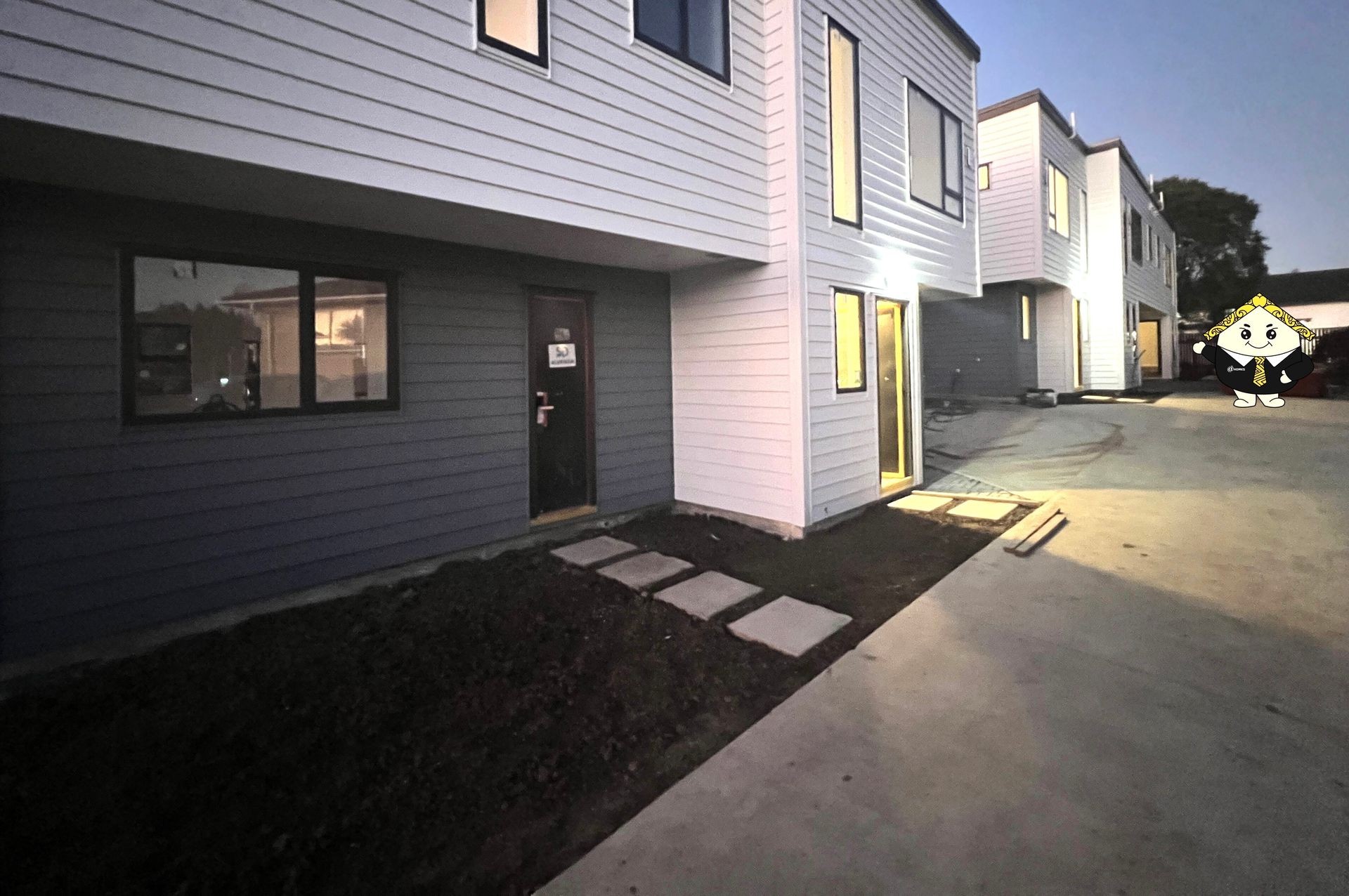 Exterior of modern townhouses at dusk with walkway and cartoon character on the right.